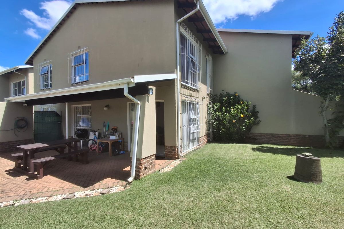Rear view of the townhouse featuring a covered brick-paved patio area and a private garden space with established lawn.