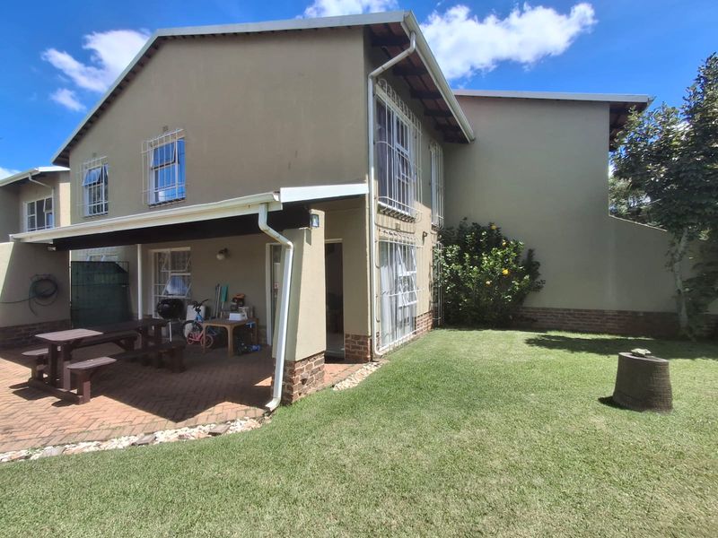 Rear view of the townhouse featuring a covered brick-paved patio area and a private garden space with established lawn.
