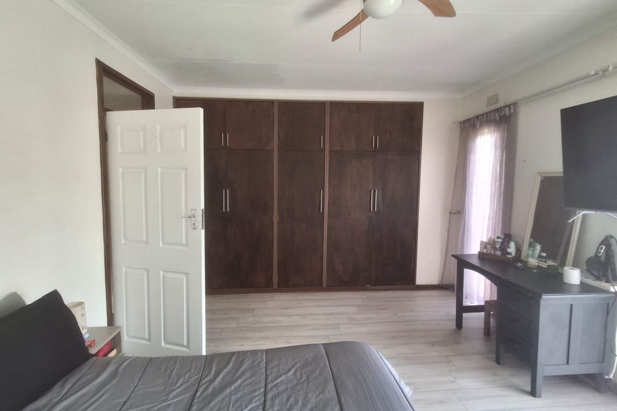 Spacious bedroom featuring light laminate flooring, extensive dark wood built-in cupboards, and a ceiling fan.