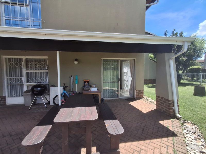A covered patio area featuring brick paving, sliding door access to the interior, and a brick-based support pillar overlooking the garden.