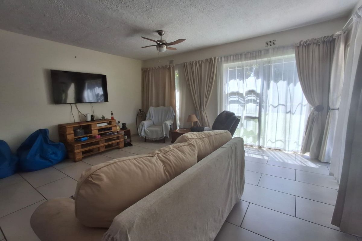 A living room featuring tiled flooring, a ceiling fan, and a large sliding glass door providing natural light and access to the exterior.