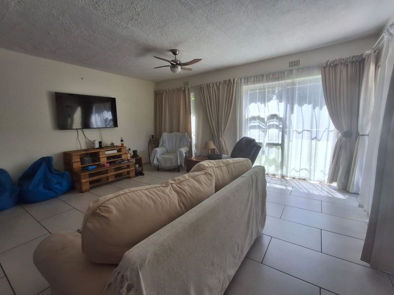 A living room featuring tiled flooring, a ceiling fan, and a large sliding glass door providing natural light and access to the exterior.