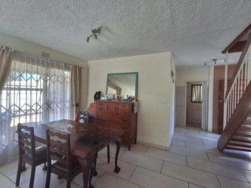 Open plan living and dining area featuring tiled flooring, a wooden staircase, and access to a security-gated patio.