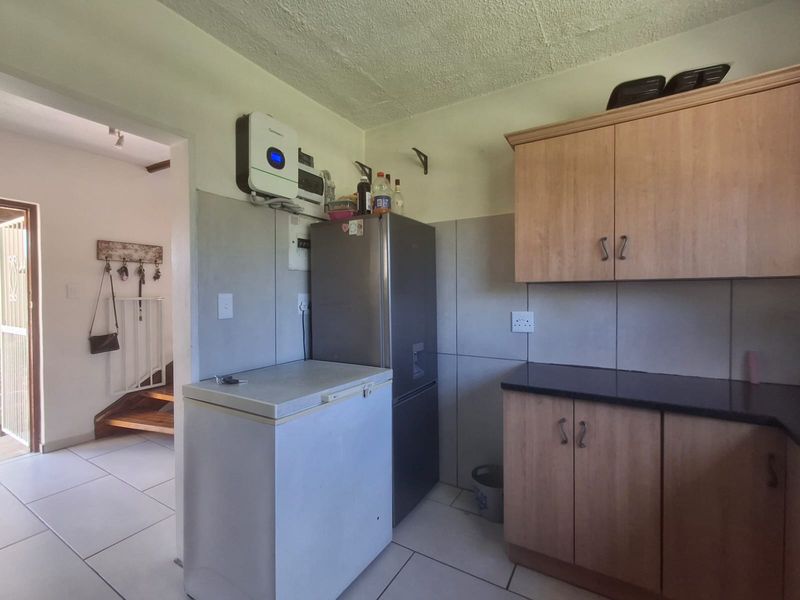 A functional kitchen area featuring built-in wooden cabinetry, dark countertops, tiled flooring, and a wall-mounted inverter system.
