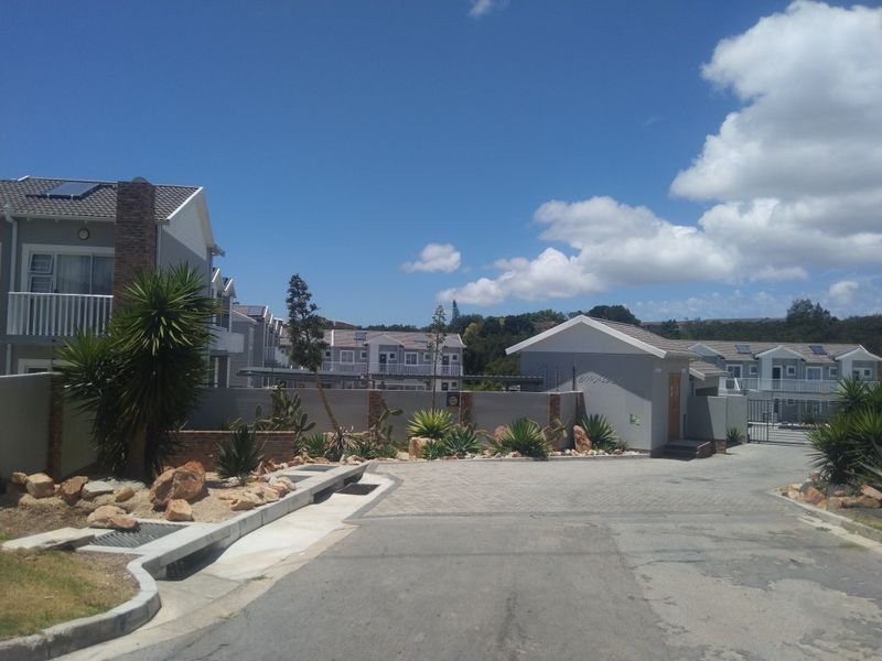 View of the apartment complex entrance featuring a paved driveway, security gate, and well-maintained perimeter wall with landscaped garden beds.