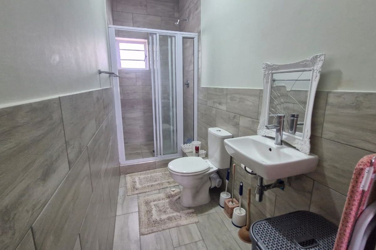 A functional bathroom featuring a shower enclosure, wall-mounted basin, and tiled finishes throughout.