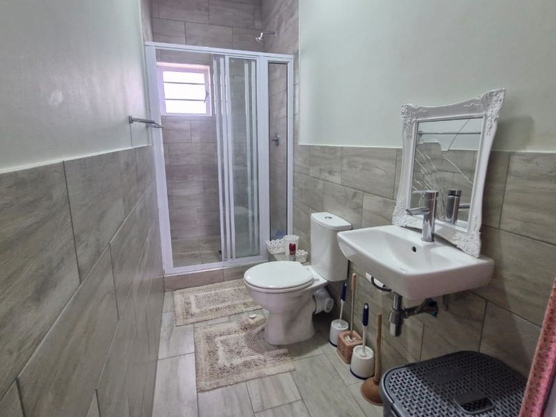 A functional bathroom featuring a shower enclosure, wall-mounted basin, and tiled finishes throughout.