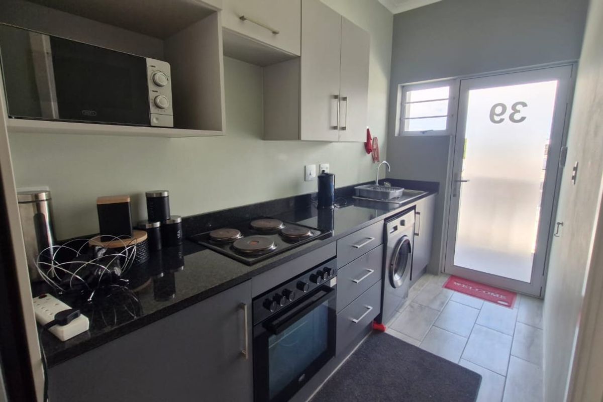 Modern galley-style kitchen featuring dark cabinetry, granite countertops, integrated appliances, and direct access to an exterior door.