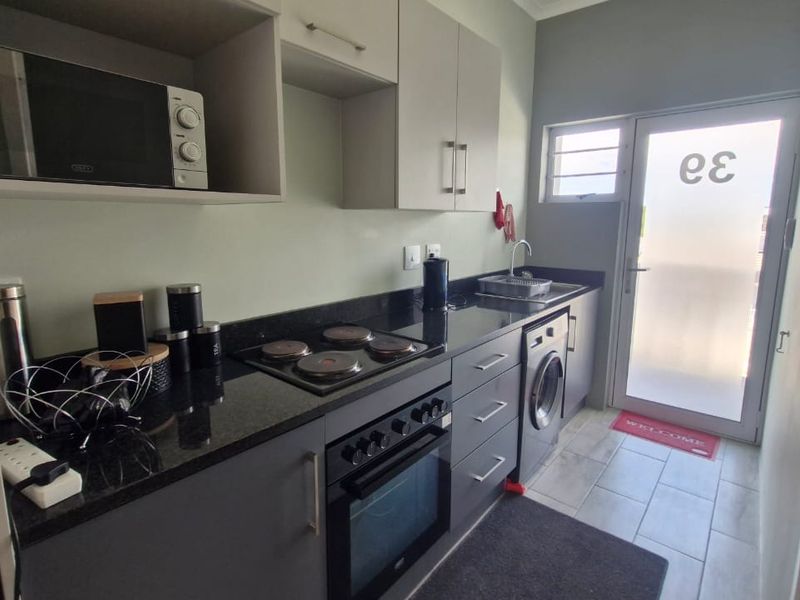 Modern galley-style kitchen featuring dark cabinetry, granite countertops, integrated appliances, and direct access to an exterior door.