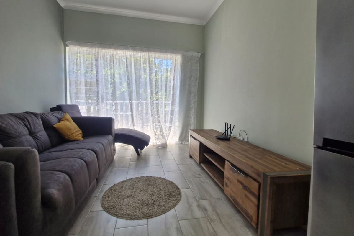 A bright living room featuring neutral wall tones, tiled flooring, and a large sliding glass door providing natural light and access to the balcony.