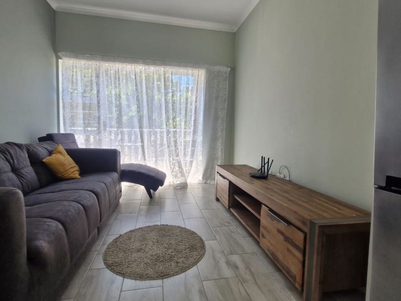 A bright living room featuring neutral wall tones, tiled flooring, and a large sliding glass door providing natural light and access to the balcony.