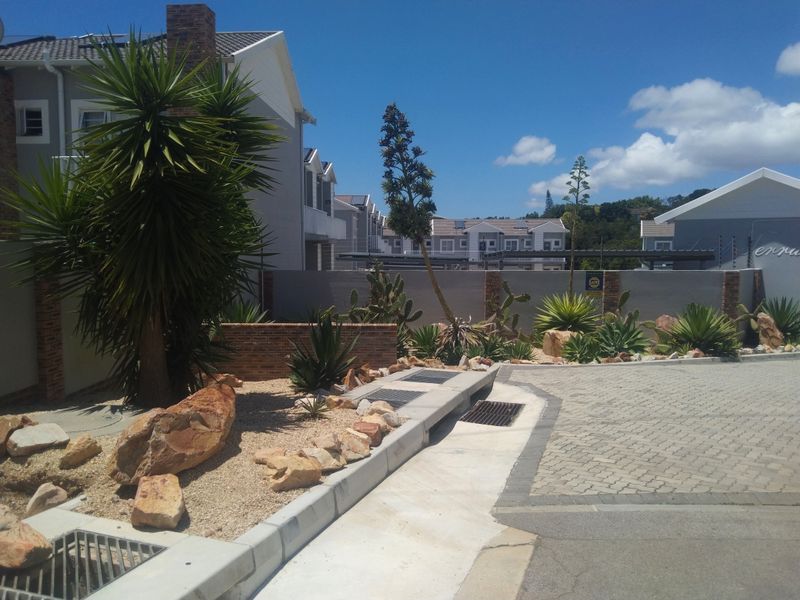 A well-maintained exterior front area featuring a paved driveway, concrete curbing, integrated stormwater drainage, and landscaped garden beds with brick boundary walls.