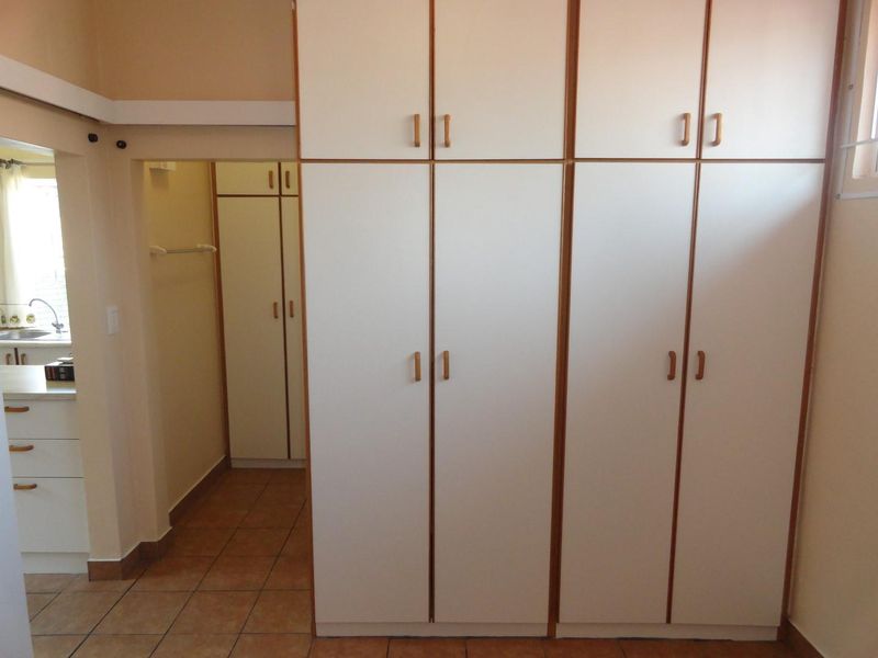 A bedroom featuring floor-to-ceiling built-in cupboards and tiled flooring, with a view into an adjacent kitchen area.