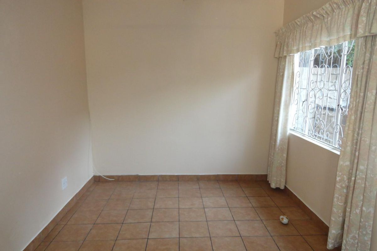 An empty bedroom featuring neutral wall paint, tiled flooring, and a window fitted with security bars.