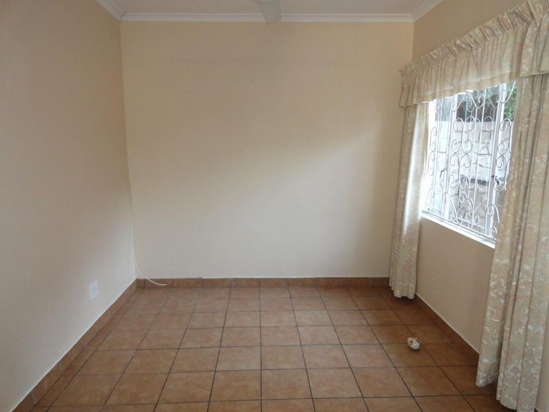 An empty bedroom featuring neutral wall paint, tiled flooring, and a window fitted with security bars.