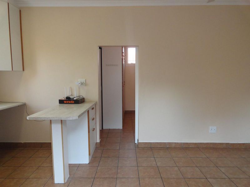 A functional kitchen area featuring tiled flooring, built-in cabinetry, and a breakfast bar, leading into an adjacent hallway.