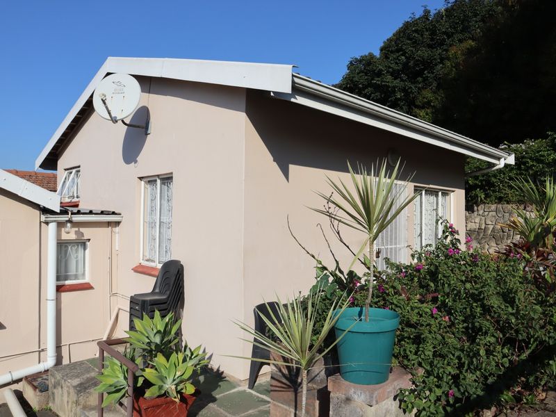 Rear exterior view of the cottage featuring a satellite dish, security bars on windows, and a stone retaining wall in the garden area.