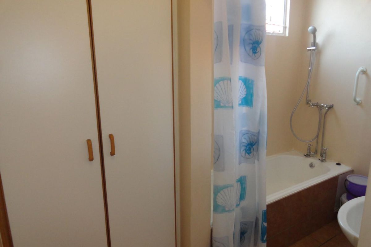 A functional bathroom featuring a built-in cupboard, a bathtub with a shower mixer, and a safety grab rail.