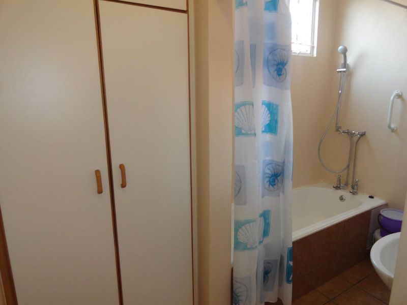 A functional bathroom featuring a built-in cupboard, a bathtub with a shower mixer, and a safety grab rail.