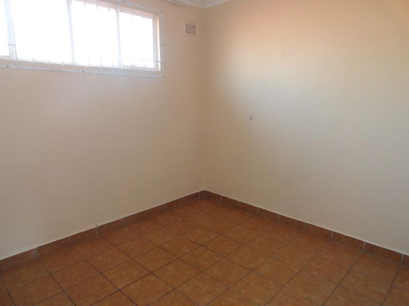 A clean, empty bedroom featuring neutral walls, tiled flooring, and a window fitted with security bars.