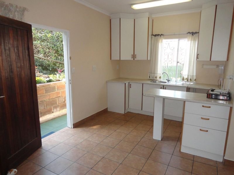A functional kitchen featuring white built-in cabinetry, laminate countertops, and tiled flooring, with direct access to an outdoor patio area.