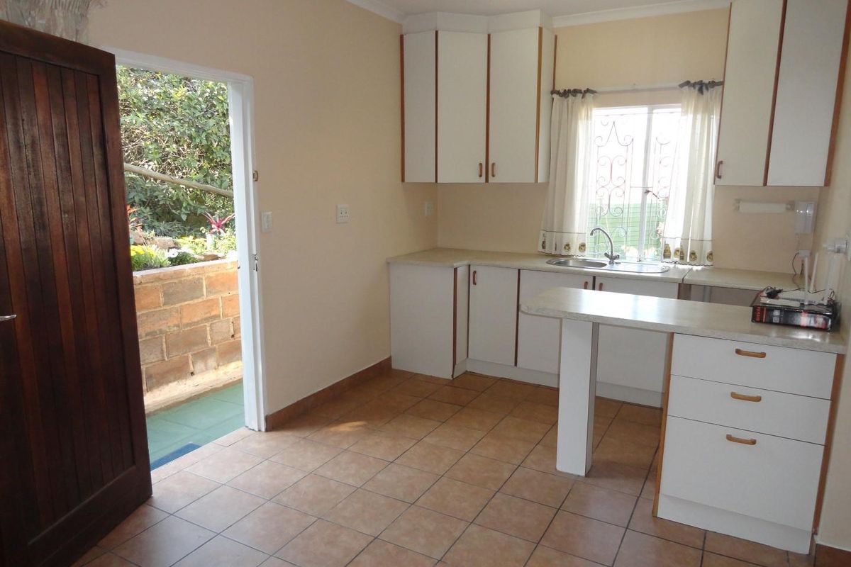 A functional kitchen featuring white built-in cabinetry, laminate countertops, and tiled flooring, with direct access to an outdoor patio area.