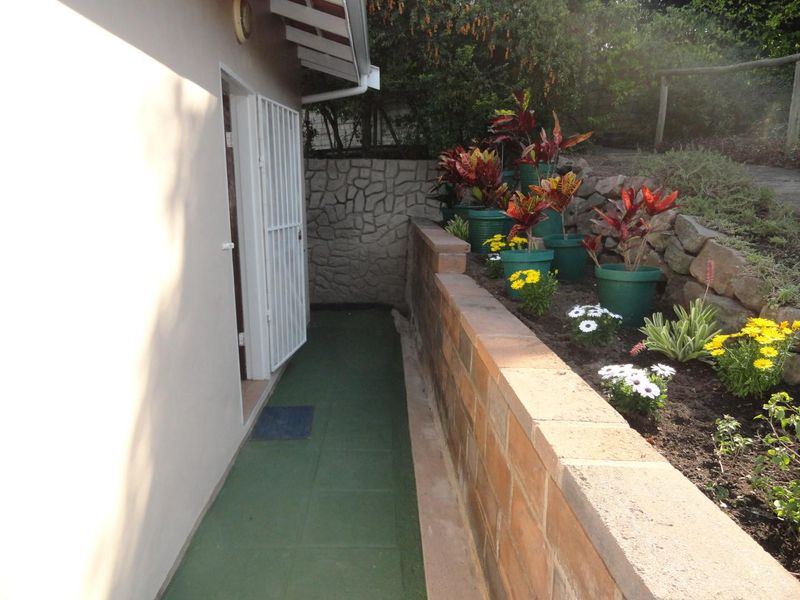 A well-maintained rear exterior pathway featuring a brick retaining wall, stone cladding accents, and a secure entrance gate.
