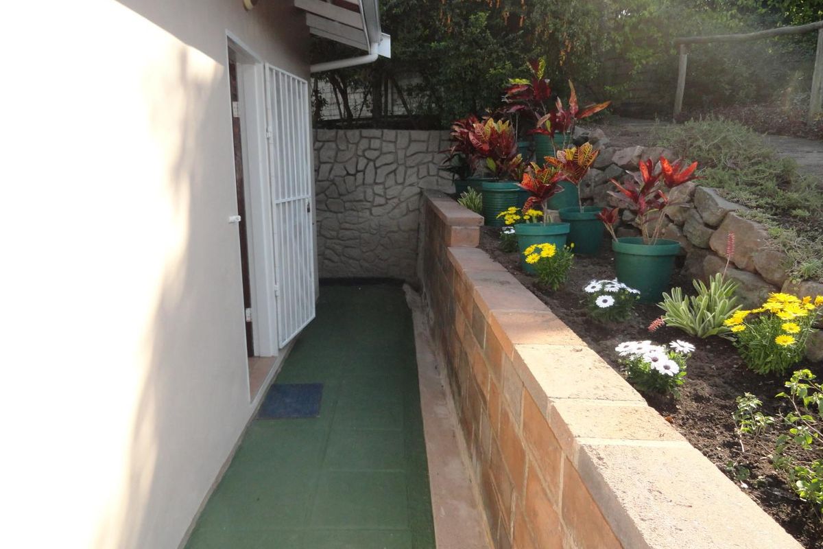 A well-maintained rear exterior pathway featuring a brick retaining wall, stone cladding accents, and a secure entrance gate.