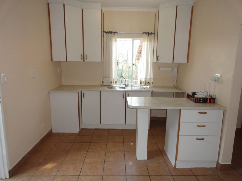 A functional kitchen featuring white built-in cabinetry, laminate countertops, a stainless steel sink, and tiled flooring, offering a clean and practical workspace.