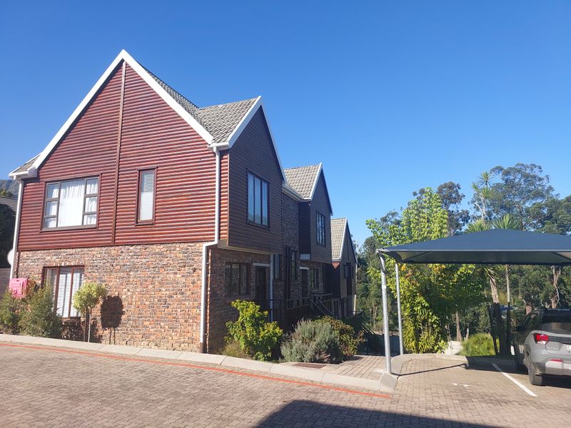 Front elevation of a multi-story townhouse featuring a combination of brick and timber cladding, a tiled roof, and a dedicated carport.