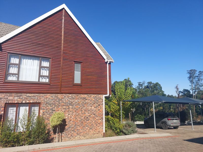 Exterior view of a townhouse featuring a combination of timber cladding and face brick facade, with an adjacent carport and paved driveway.