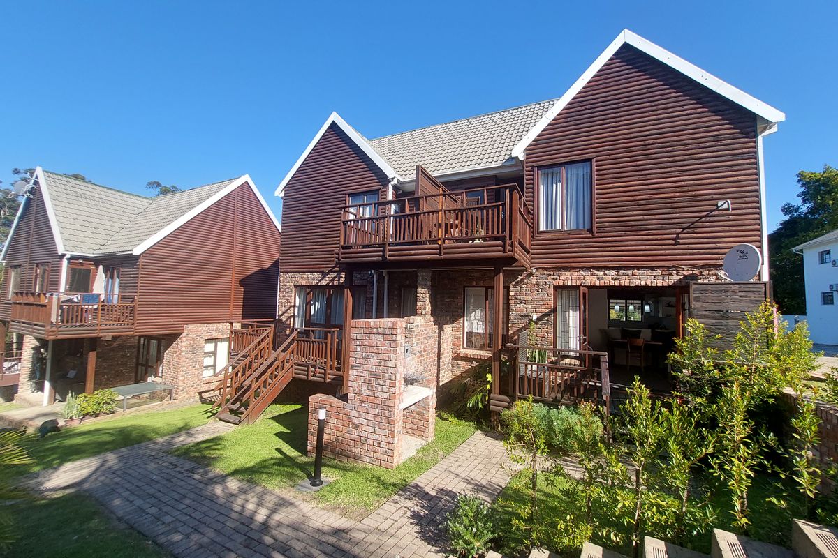 Rear view of a multi-level townhouse featuring timber cladding, brick accents, a private balcony, and a built-in outdoor braai area.