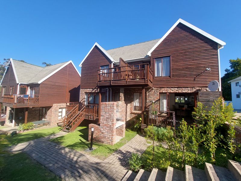 Rear view of a multi-level townhouse featuring timber cladding, brick accents, a private balcony, and a built-in outdoor braai area.