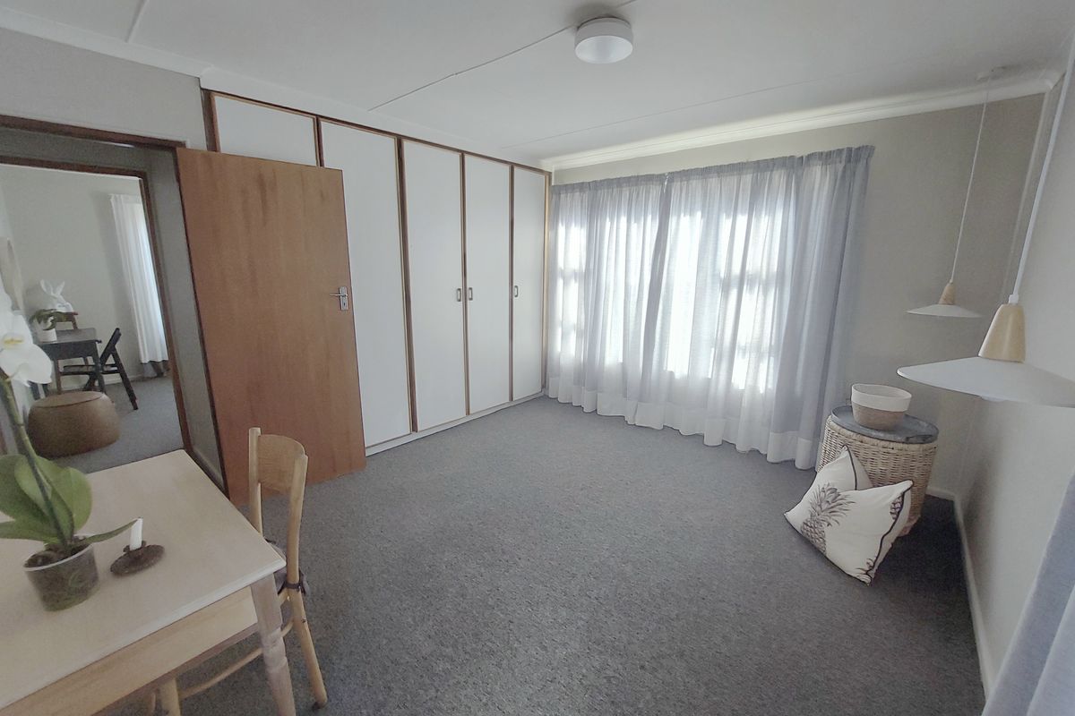 A bedroom featuring built-in cupboards, carpeted flooring, and natural light through window curtains.