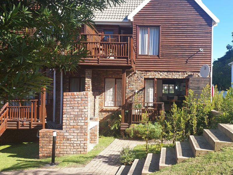 Rear view of a two-story townhouse featuring log cabin style cladding, a brick facade, a wooden balcony, and a built-in brick braai area.