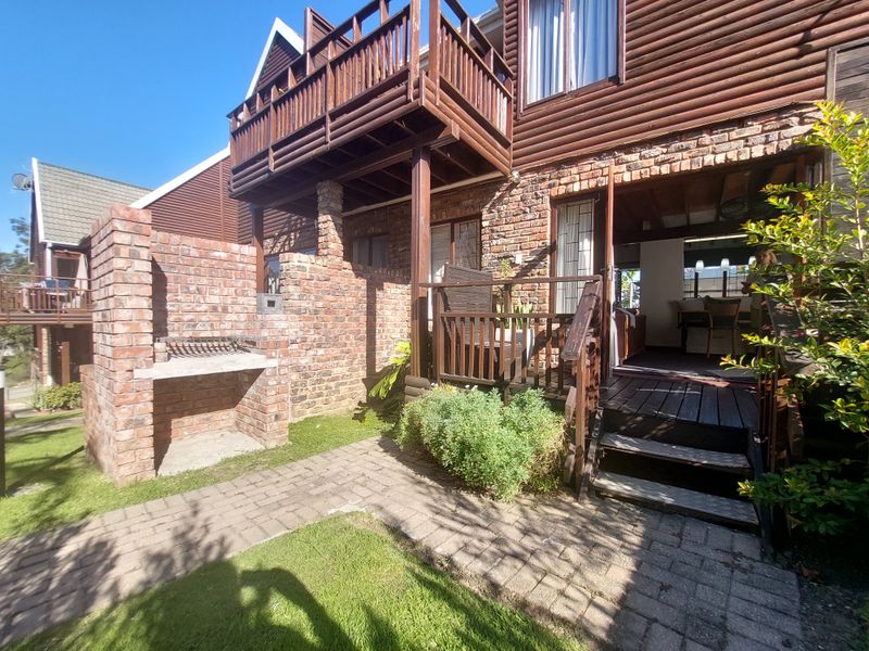 Rear view of the townhouse featuring a brick braai area, timber balcony, and wooden deck leading into the living space.