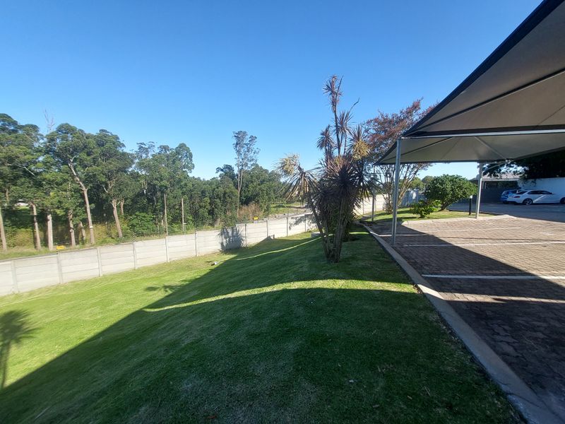 A view of the rear exterior area featuring a paved driveway with a shade cloth carport, a well-maintained lawn, and a precast boundary wall.