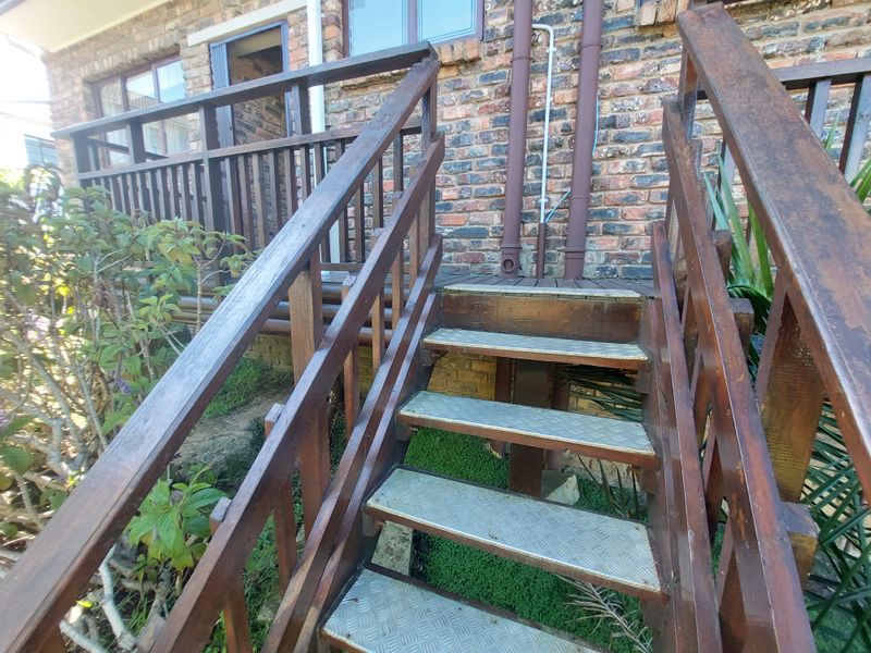 Exterior rear view showing a timber staircase with metal tread plates leading to a raised deck area against a brick townhouse facade.