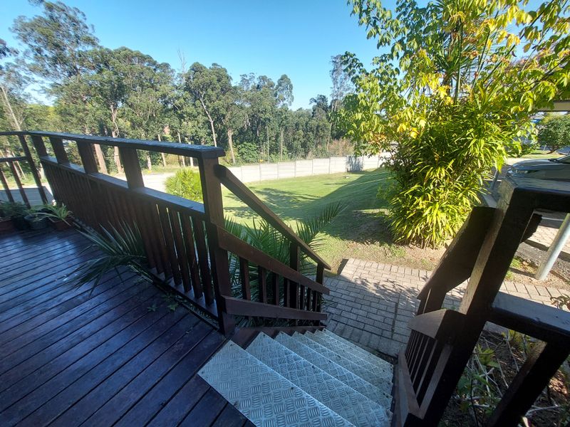 Elevated timber deck with balustrade and metal staircase leading down to a paved walkway and private garden area.