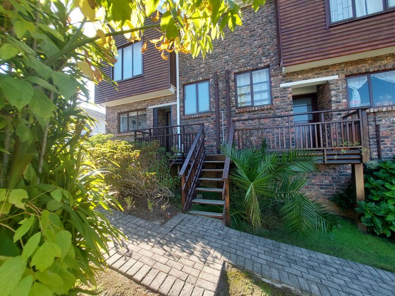 Rear exterior view of the townhouse featuring a brick facade, timber cladding, and a raised timber deck with stairs leading to the garden.