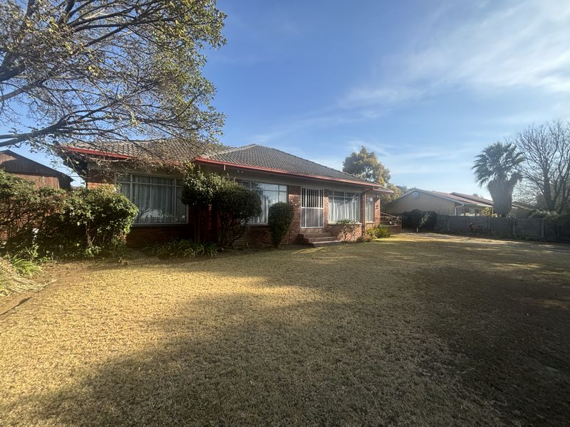 A front view of a single-story brick house featuring a tiled roof, large windows, and a spacious front lawn.