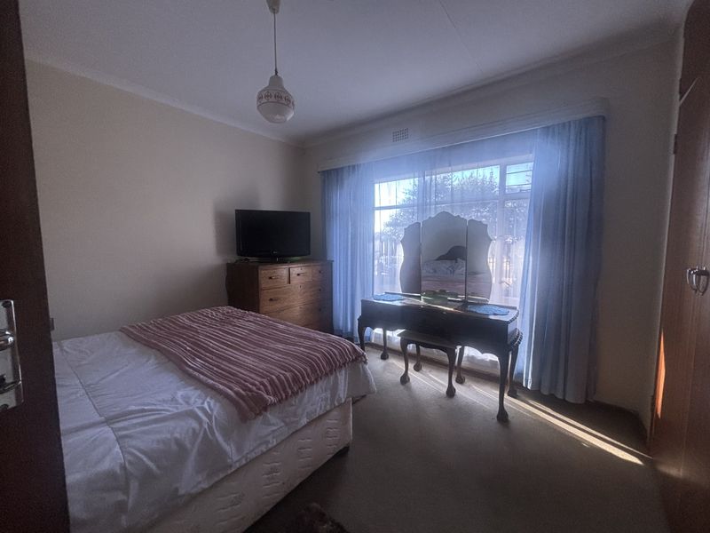 A functional bedroom featuring carpet flooring, a large window with natural light, and a built-in wardrobe.