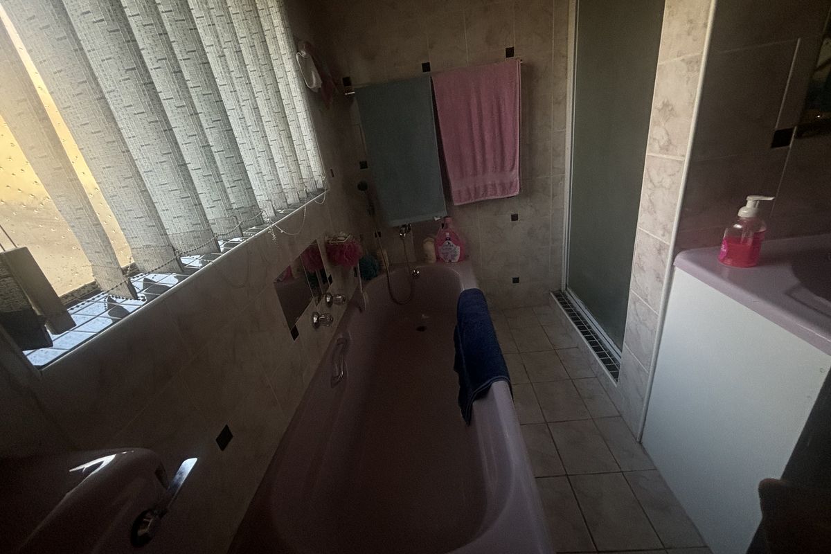A dated bathroom featuring a pink bathtub, separate shower enclosure, and tiled finishes. The space would benefit from modern updates to fixtures and decor.