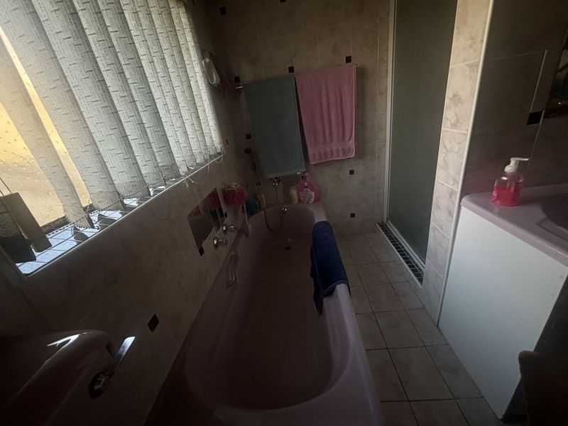 A dated bathroom featuring a pink bathtub, separate shower enclosure, and tiled finishes. The space would benefit from modern updates to fixtures and decor.