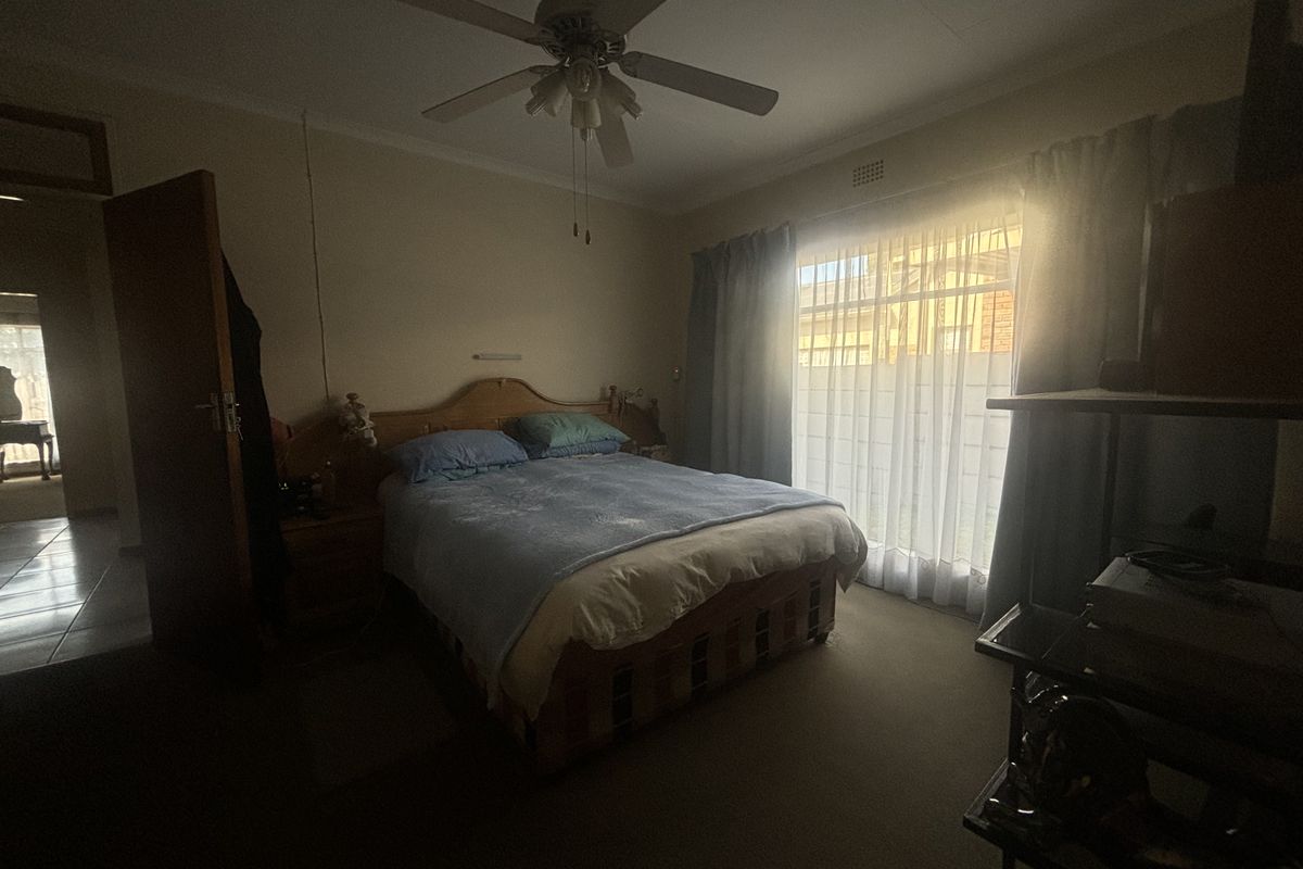 A standard bedroom featuring a ceiling fan and large window with curtain rails, providing natural light and access to the exterior.