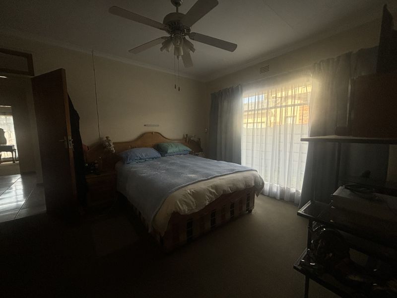 A standard bedroom featuring a ceiling fan and large window with curtain rails, providing natural light and access to the exterior.