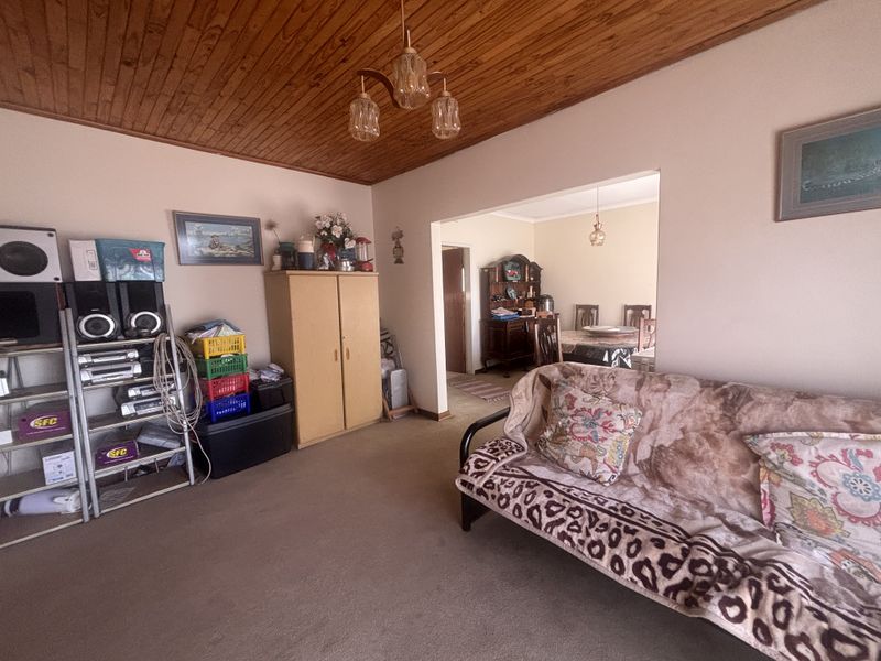 A living room featuring a timber tongue and groove ceiling and carpeted flooring, with an open transition to the adjacent dining area.