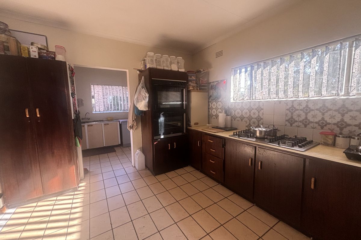 A functional kitchen featuring built-in cabinetry, a gas hob, and an integrated oven, with a separate scullery area visible through the doorway.