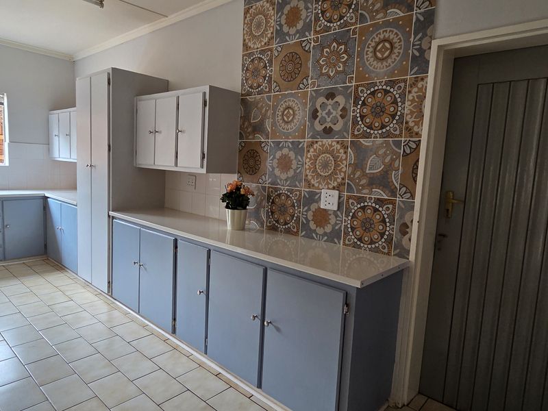 Functional kitchen featuring ample built-in cabinetry, decorative tiled splashback, laminate countertops, and durable ceramic floor tiles.