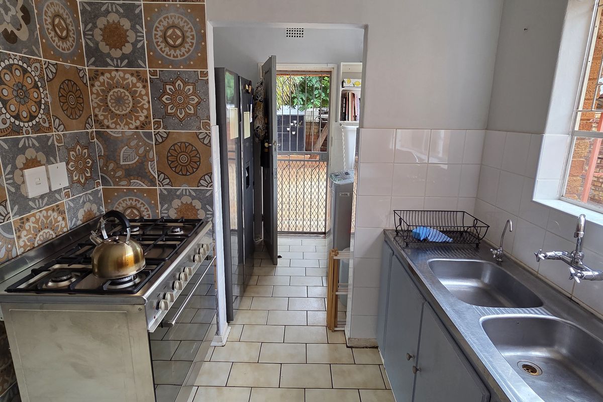 Functional kitchen featuring a gas stove, stainless steel double sink, and decorative tiled splashback with direct access to the rear exterior.